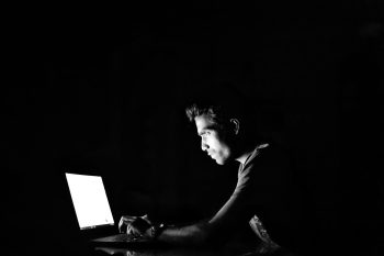 A man sitting in the dark, using a laptop.