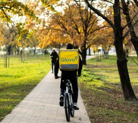 A Glovo worker cycling through a park.